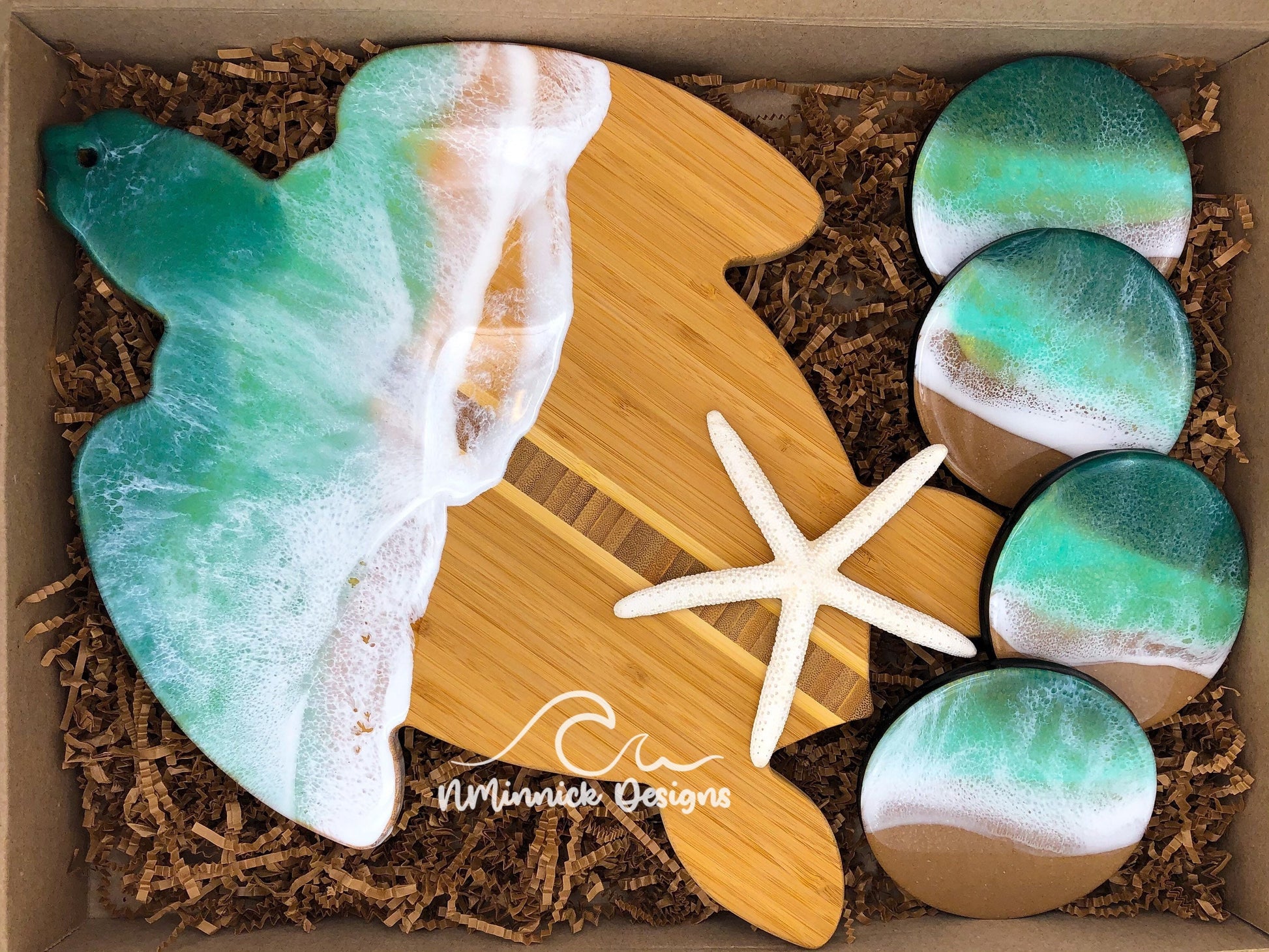 sea turtle-shaped bamboo charcuterie board. Top portion covered in dark green and light green ocean resin art resembling the waves of the ocean. Matching set of 4 round ocean resin drink coasters with real sand and cork backings. Shown packaged in a kraft colored eco-friendly and plastic free gift box with a free Happy Birthday card.