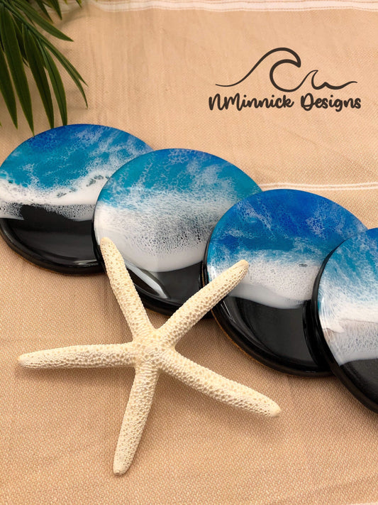 handmade coaster set of 4 with a black sand beach and blue and white ocean waves made of epoxy resin. cork backings.