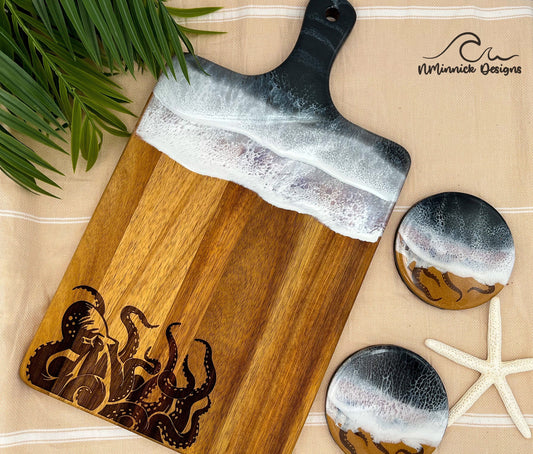 Acacia wood serving board with handle.  Top portion coated in black and silver ocean resin art resembling the waves of the ocean.  Bottom portion laser engraved with an octopus.  Matching set of 2 ocean resin and laser engraved octopus drink coasters.  Laying on a tan beach towel next to a natural starfish (not included).