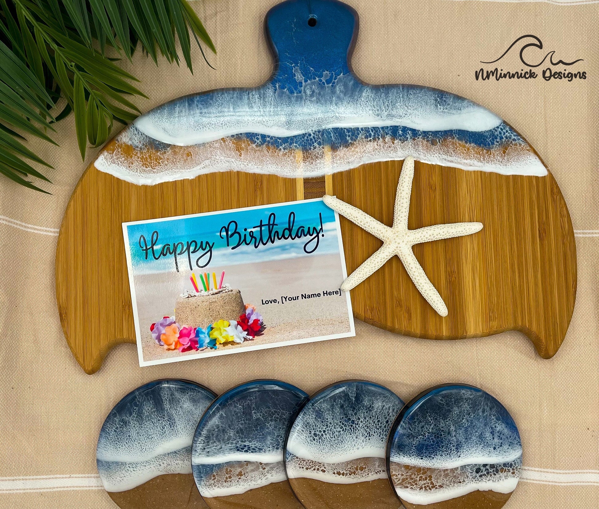 Whale Fin-shaped bamboo charcuterie board with top portion covered in dark and medium blue ocean resin art resembling the waves of the ocean.  Matching set of 4 ocean resin drink coasters with cork backing and a free personalized Happy Birthday Card.
