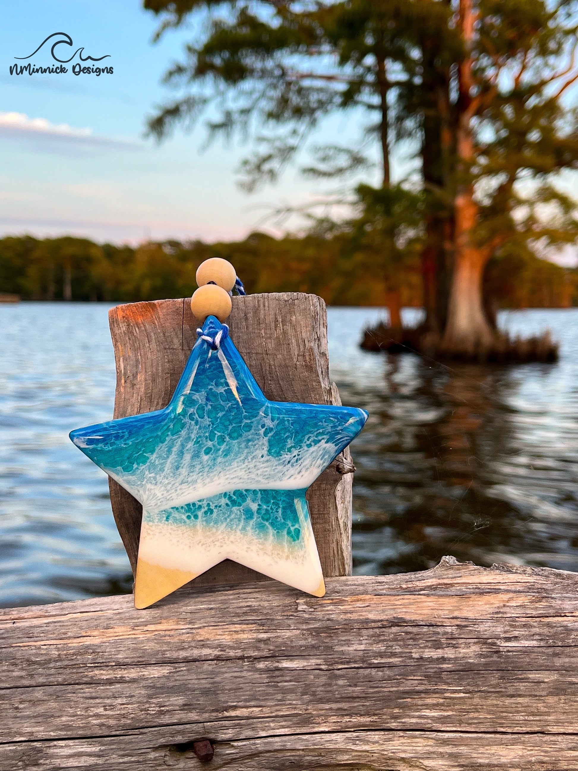 Star-shaped wooden Christmas ornament covered in blue and teal ocean resin art resembling the waves of the ocean.  Finished with blue and white baker's twine and two wooden beads
